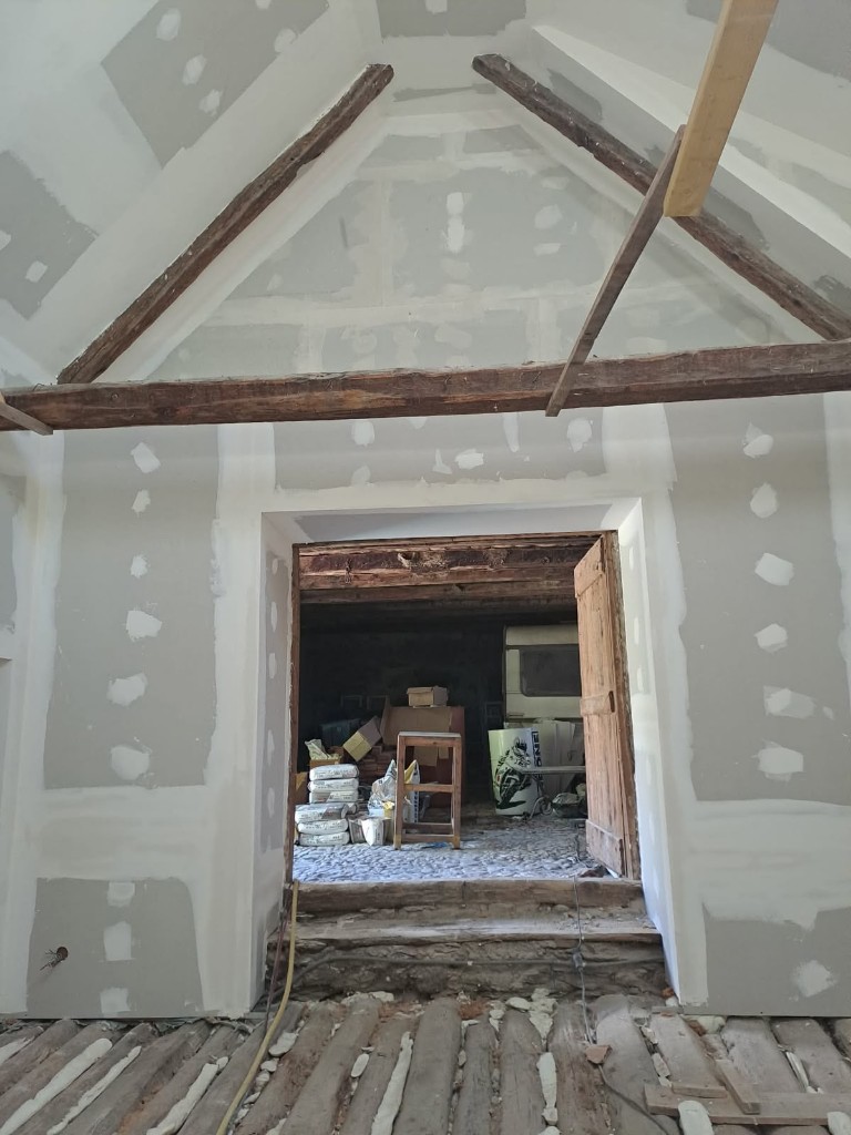 Rénovation intérieure en cours : pose de plaques de plâtre et poutres apparentes sous plafond voûté